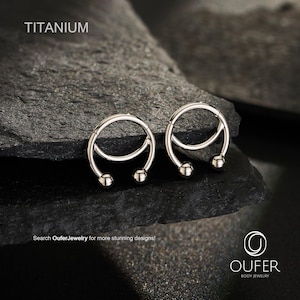 May include: Two silver-colored titanium circular body jewelry rings with a hinged segment and a small ball at each end. The text TITANIUM is visible in the top left corner, and the text OUFER BODY JEWELRY is in the bottom right corner.