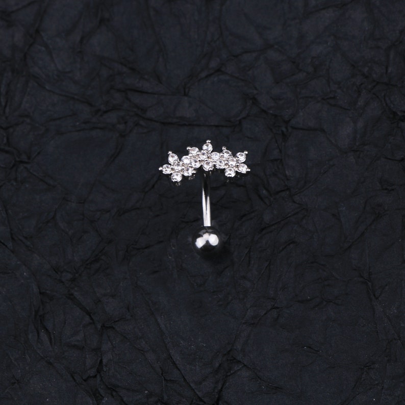 May include: A silver belly button ring with a clear crystal flower design.
