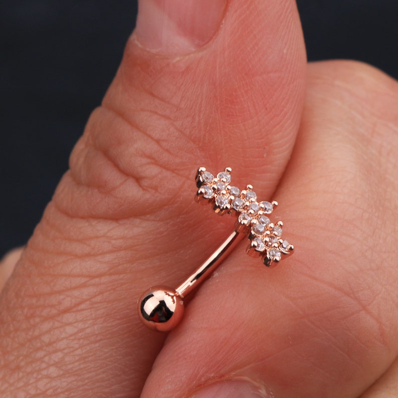 May include: Rose gold belly button ring with a clear crystal flower design.
