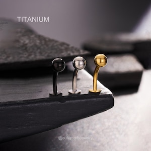 Puede incluir: Tres piezas de joyería corporal de titanio con barras curvas y extremos de bola. Las piezas son en oro, plata y negro.