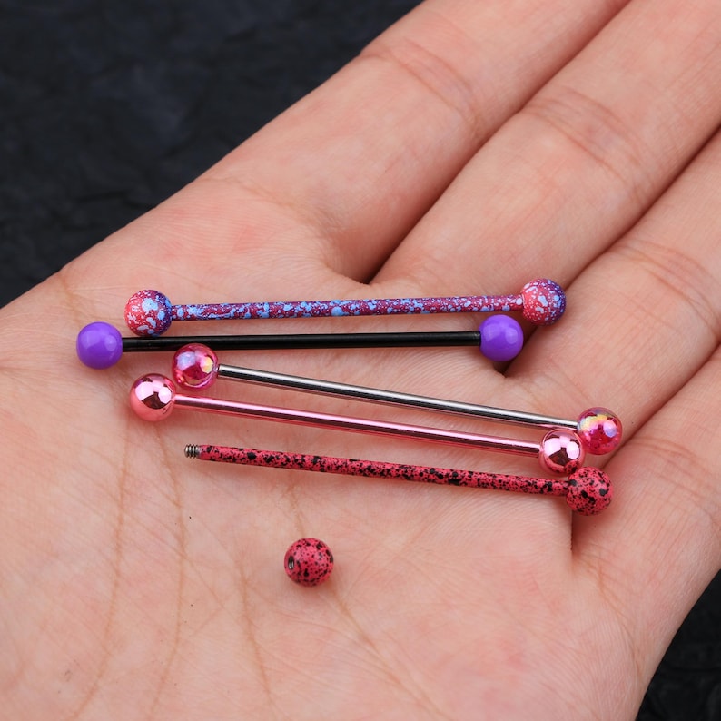May include: Five different barbell style body jewelry pieces with colorful balls. The balls are pink, purple, and blue with white speckles. The barbells are silver, black, and pink.