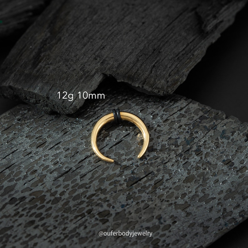 May include: Gold 10mm 12 gauge septum ring with black o-rings. The ring is on a black background.