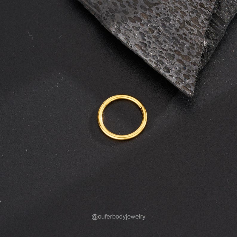 May include: A gold-colored seamless ring for body piercing. The ring is circular and has a smooth, polished finish.
