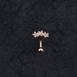 May include: A rose gold belly button ring with a clear crystal flower design.