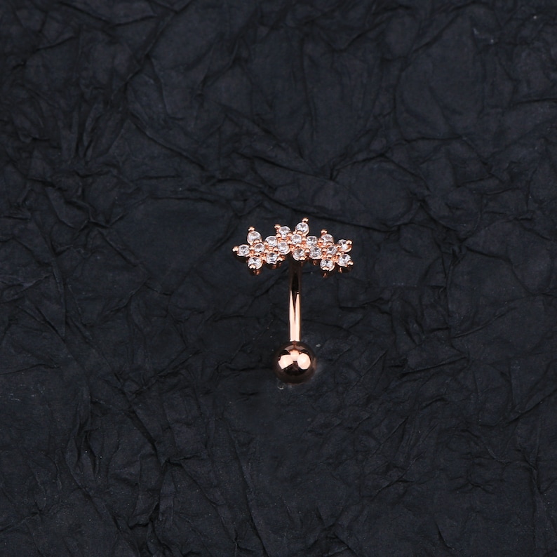 May include: A rose gold belly button ring with a clear crystal flower design.