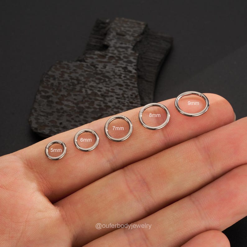 Puede incluir: Un conjunto de seis anillos plateados sin costuras de diferentes tama&ntilde;os, que van de 5 mm a 9 mm. Los anillos se muestran en una mano, con cada anillo etiquetado con su di&aacute;metro en mil&iacute;metros.