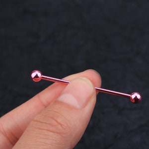 May include: A pink barbell with rounded ends. The barbell is made of metal and is about 2 inches long.