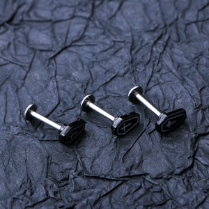 May include: Three silver body jewelry pieces with black coffin-shaped charms. Each charm has a small white cross on it.