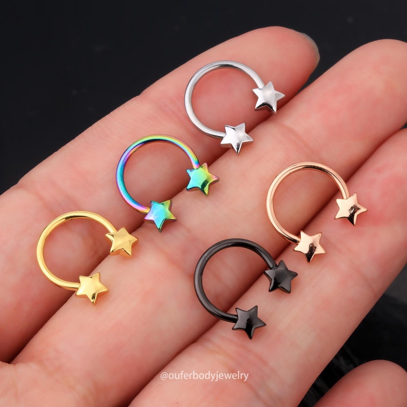 May include: Five different colored horseshoe shaped rings with two star-shaped charms on each ring. The rings are silver, rainbow, gold, rose gold, and black.