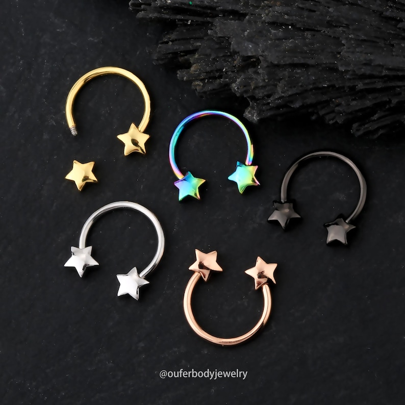 May include: Five horseshoe shaped body jewelry pieces with star-shaped charms. The jewelry is available in gold, rainbow, silver, black, and rose gold.