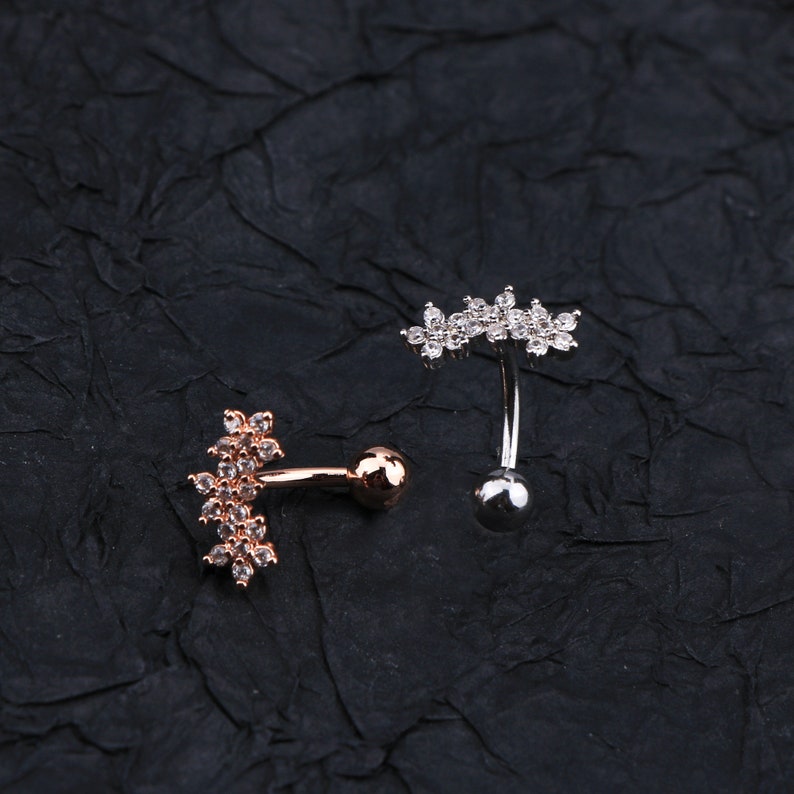 May include: Two belly button rings with clear crystal flower accents. One ring is silver and the other is rose gold.