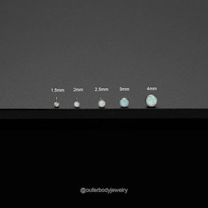 Op de afbeelding: Vijf opal body jewelry-stukken in verschillende maten, van 1,5 mm tot 4 mm. De sieraden worden weergegeven op een zwart oppervlak met de maten eronder.