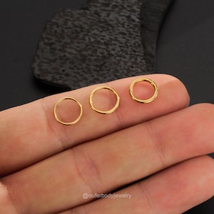 May include: Three gold seamless rings for body piercing. The rings are different sizes and are shown on a hand.
