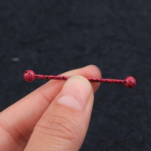 May include: A red and black barbell with rounded ends. The barbell is made of metal and has a speckled finish.