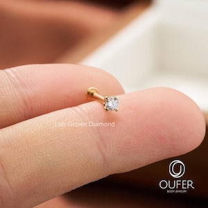 Puede incluir: Un pendiente de bot&oacute;n de diamante cultivado en laboratorio de color dorado. El pendiente presenta un peque&ntilde;o diamante de talla cuadrada engastado en un poste plano. El texto "Lab Grown Diamond" es visible. El pendiente se sostiene entre dos dedos.