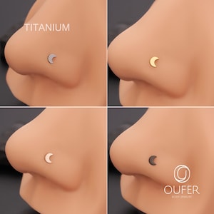 May include: Nose studs with a crescent moon design in silver, gold, and black. The word "TITANIUM" is visible. The brand "OUFER BODY JEWELRY" is displayed. The image showcases body jewellery, with a focus on the moon-shaped studs.