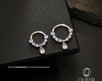 May include: Two silver-toned circular hoop rings featuring a series of small, light purple circular stones along the lower half and a single pear-shaped light purple stone dangling from the center. Text reads: Search OuferJewelry for more stunning designs!