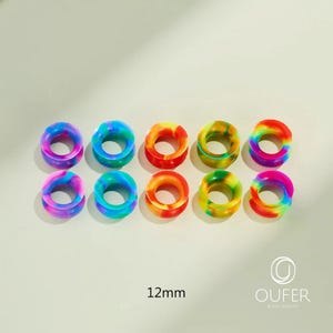 May include: Ten colorful, rainbow-colored ear gauges. Each gauge is a circular tunnel design, with a 12mm diameter. The gauges are in shades of blue, green, yellow, orange, and pink. The brand name "OUFER BODY JEWELRY" is in the bottom right corner.