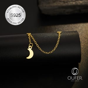Puede incluir: Una cadena de cuerpo dorada con un colgante de media luna. La cadena está conectada a una pequeña cadena con un dije de luna. La imagen también muestra un sello de plata de ley S925.