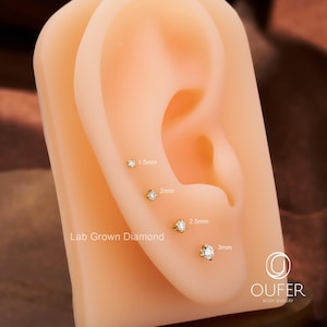 Puede incluir: Exhibici&oacute;n de pendientes de diamantes cultivados en laboratorio en varios tama&ntilde;os: 1,5 mm, 2 mm, 2,5 mm y 3 mm. Los pendientes son de oro y se muestran en una oreja de maniqu&iacute;. El texto "Lab Grown Diamond" es visible.