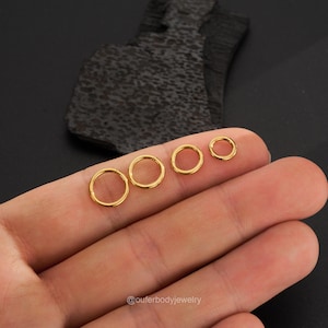 May include: Five gold seamless rings of different sizes, displayed on a hand. The rings are made of surgical steel and are available in various sizes.