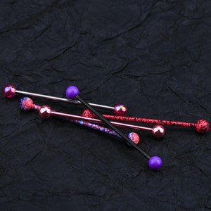 May include: Four different barbell piercings with colorful balls. The barbells are made of metal and have a black, silver, and pink finish. The balls are purple, pink, and iridescent.