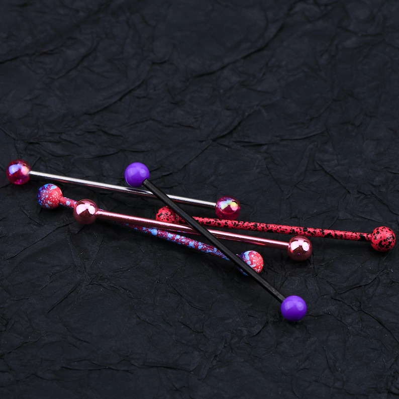 May include: Four different barbell piercings with colorful balls. The barbells are made of metal and have a black, silver, and pink finish. The balls are purple, pink, and iridescent.