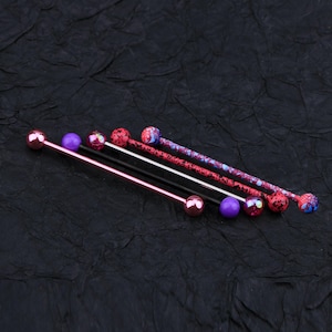 May include: Four different barbell piercings with colorful balls. The barbells are made of metal and have a variety of colors, including pink, purple, and black. The balls are also colorful and have a variety of designs.