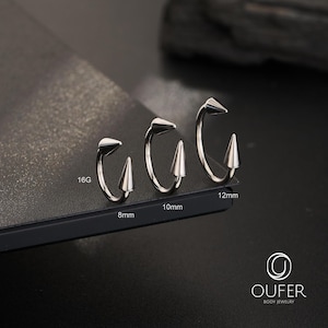 May include: Three silver-toned circular body jewelry pieces with pointed cone ends. The rings are labeled with sizes 8mm, 10mm, and 12mm, and a gauge size of 16G. The brand name OUFER BODY JEWELRY is printed in the bottom right corner of the image.