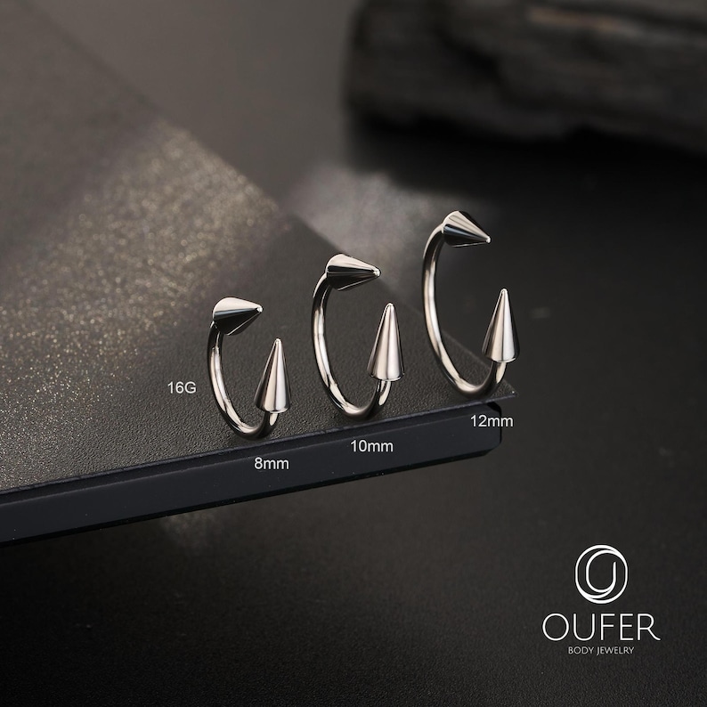 May include: Three silver-toned circular body jewelry pieces with pointed cone ends. The rings are labeled with sizes 8mm, 10mm, and 12mm, and a gauge size of 16G. The brand name OUFER BODY JEWELRY is printed in the bottom right corner of the image.