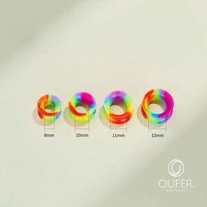 May include: Four rainbow-colored ear gauges in varying sizes: 8mm, 10mm, 11mm, and 12mm. Each gauge features a vibrant blend of colors, including red, orange, yellow, green, blue, and purple. The gauges are made of a smooth material.