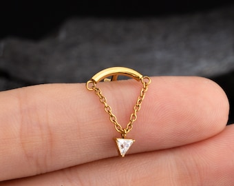 Peut inclure: Bijou de corps en or avec une barre incurvée et une chaîne pendante se terminant par un bijou transparent en forme de triangle.