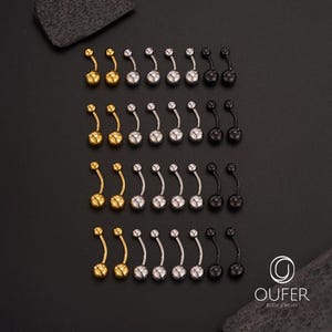 May include: An assortment of belly button rings in gold, silver, and black. Each curved barbell features a small, round ball on the top and a larger, matching ball at the bottom. The jewelry is displayed on a black surface.