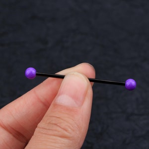 May include: A black barbell with purple balls on each end. The barbell is about 3 inches long.