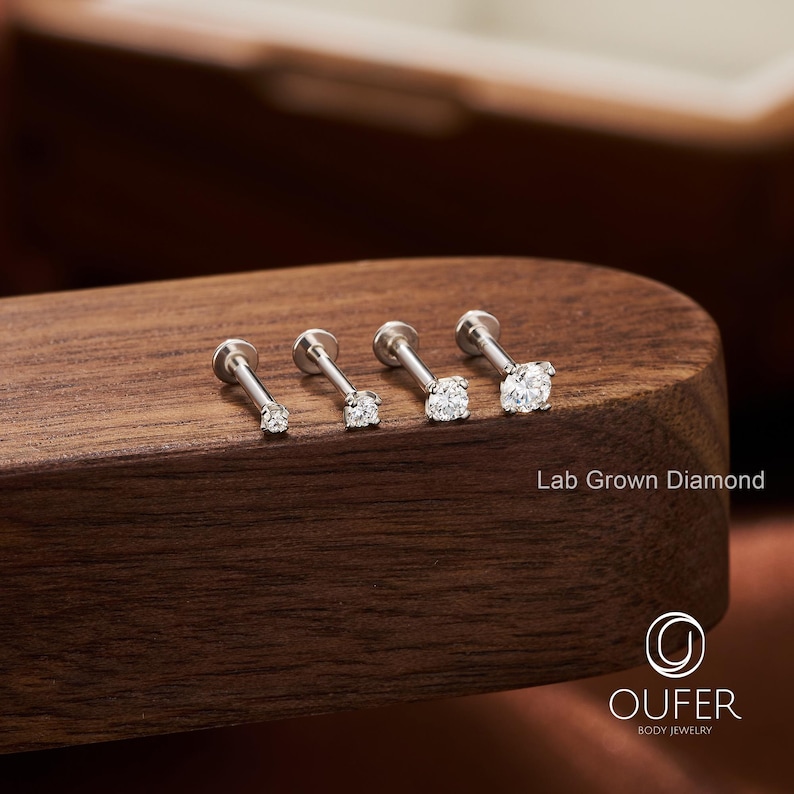 Puede incluir: Cuatro pendientes labret de plata con diamantes redondos cultivados en laboratorio, transparentes, de diferentes tama&ntilde;os. Las joyas se exhiben sobre una superficie de madera oscura. El texto "Lab Grown Diamond" es visible.