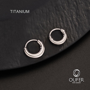 Puede incluir: Dos pendientes de aro de titanio plateado. Los pendientes tienen forma de media luna y un acabado pulido. La palabra "TITANIUM" est&aacute; impresa en blanco en la parte superior izquierda. Los pendientes se muestran sobre una superficie oscura. La marca "OUFER BODY JEWELRY" est&aacute; impresa en la parte inferior derecha.