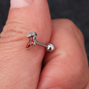 May include: A silver Christmas stocking charm with red and clear rhinestones. The charm is attached to a silver barbell post.