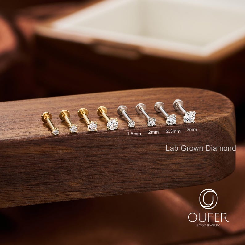 Puede incluir: Una colecci&oacute;n de pendientes de diamantes cultivados en laboratorio de varios tama&ntilde;os, exhibidos sobre una superficie de madera. Los pendientes son en tonos dorados y plateados, con piedras claras y brillantes. Tama&ntilde;os de 1,5 mm a 3 mm. Texto "Lab Grown Diamond".