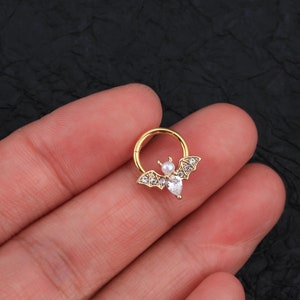 Puede incluir: Joyer&iacute;a corporal en forma de murci&eacute;lago de tono dorado con diamantes de imitaci&oacute;n transparentes y blancos. El murci&eacute;lago est&aacute; unido a un aro de tono dorado.