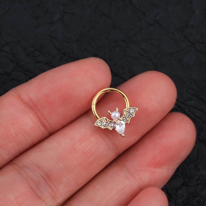 Puede incluir: Joyer&iacute;a corporal en forma de murci&eacute;lago de tono dorado con diamantes de imitaci&oacute;n transparentes y blancos. El murci&eacute;lago est&aacute; unido a un aro de tono dorado.