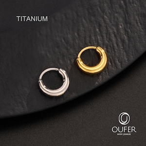 Puede incluir: Dos pendientes de aro de titanio, uno plateado y otro dorado, se muestran sobre una superficie oscura. La palabra "TITANIUM" est&aacute; impresa encima de los pendientes. Los pendientes tienen un dise&ntilde;o simple y redondeado.