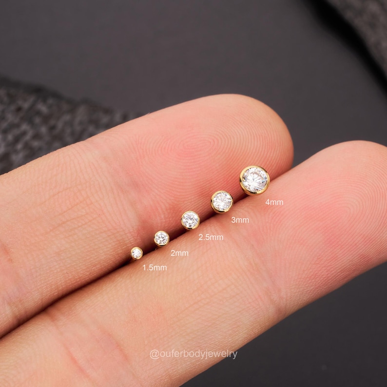 May include: A set of six gold-toned body jewelry pieces with clear round gemstones. The pieces are arranged in order of size, from 1.5mm to 4mm. The jewelry is displayed on a hand.