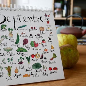 May include: A white calendar with the word "Septembre" written in black cursive. The calendar lists various fruits and vegetables in French, with hand-drawn illustrations of each item.