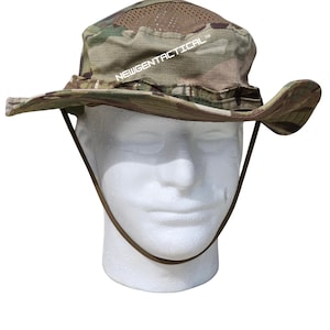 May include: A camouflage boonie hat featuring a wide brim, a mesh crown section for ventilation, and an adjustable chin strap. The text NEWGENTACTICAL is printed in white on the front of the hat, which is displayed on a white mannequin head.