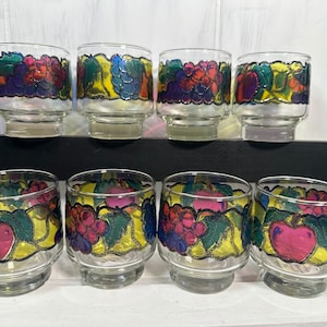 Può includere: Set di otto bicchieri di vetro trasparente con disegni di frutta colorati. Ogni bicchiere presenta un disegno dipinto di uva, mele e foglie nei toni del rosso, viola, verde e giallo. I bicchieri hanno una base corta e arrotondata.