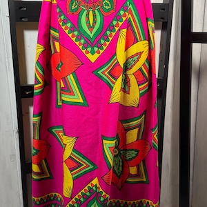 Peut inclure: Longue jupe avec une taille haute grise et des boutons décoratifs. La jupe présente un motif saisissant de fleurs et de formes géométriques en rose, vert, jaune et rouge. Le tissu est orné de motifs.