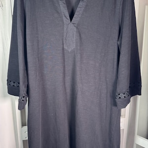 May include: Black long-sleeve dress with a V-neckline and decorative cutouts on the sleeves and hem. The dress is made of a soft, lightweight fabric and hangs on a black hanger.