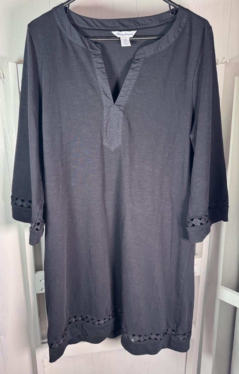 May include: Black long-sleeve dress with a V-neckline and decorative cutouts on the sleeves and hem. The dress is made of a soft, lightweight fabric and hangs on a black hanger.
