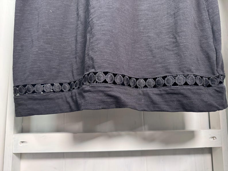 May include: A dark gray top with a decorative, circular lace trim along the bottom edge. The fabric appears to be a soft knit material. The trim is a darker shade of gray, creating a subtle contrast.