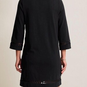 May include: A black dress with three-quarter sleeves and a V-neck. The dress features a decorative openwork trim at the sleeve cuffs and hemline. The dress is made of a soft, opaque fabric.